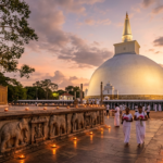 Une photographie de paysage en grand angle capturant le stupa Ruwanwelisaya illuminé à Anuradhapura au Sri Lanka pendant le coucher du soleil Des dévots vêtus de blanc avec des offrandes marchent le long dun chemin éclairé par des lampes à côté dun mur détaillé sculpté déléphants et dun arbre Bodhi sacré sous un ciel crépusculaire coloré